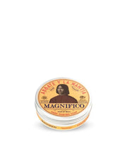 A solid shaving soap puck packaged in a round container with a lid featuring text and a portrait illustration. The label reads 'MAGNIFICO' and includes the words 'Solid Shaving Soap' as well as a list of ingredients like Eucalyptus Honey, Saffron.