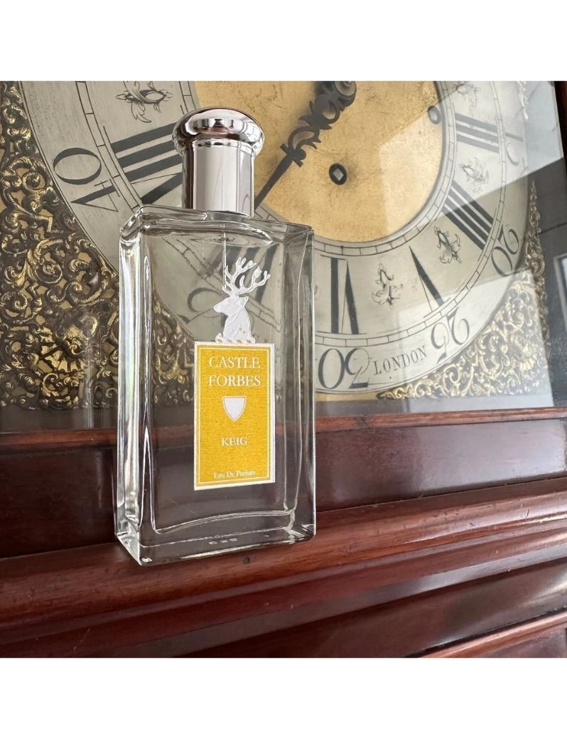 Castle Forbes Keig Eau de Parfum bottle on a wooden mantel in front of an antique clock, elegant citrus fragrance hero shot