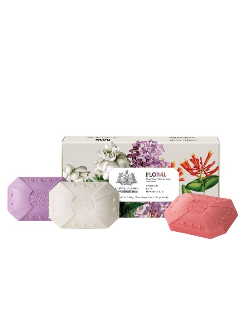 Three hexagonal bar soaps in lavender, gardenia, and honeysuckle are displayed in front of their floral-themed packaging box on a solid white background.
