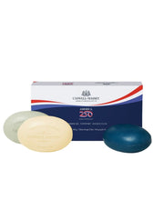 Three oval-shaped soap bars in pale green, cream, and deep blue are displayed in front of their Caswell-Massey America 250 box on a plain white background.