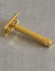 Underside view of the Fatip Classic gold razor showing the baseplate and fluted handle on a gray stone surface