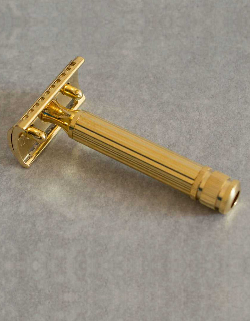 Underside view of the Fatip Classic gold razor showing the baseplate and fluted handle on a gray stone surface