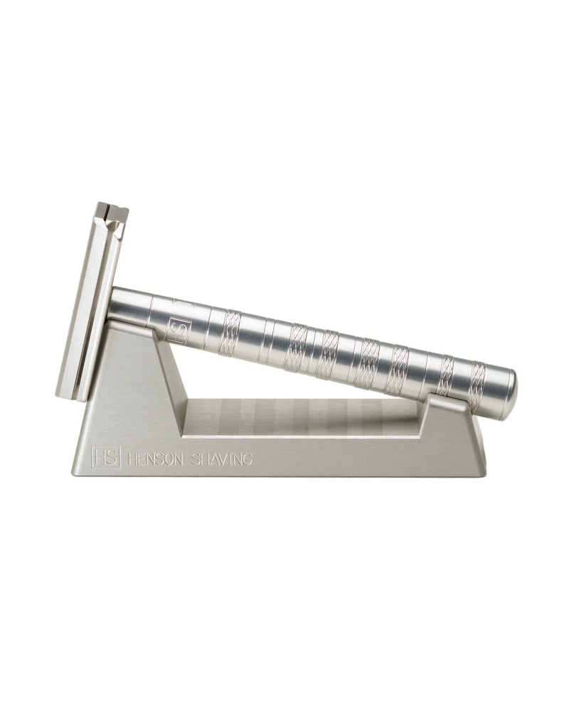A silver safety razor with a metallic finish resting on a matching metal stand.