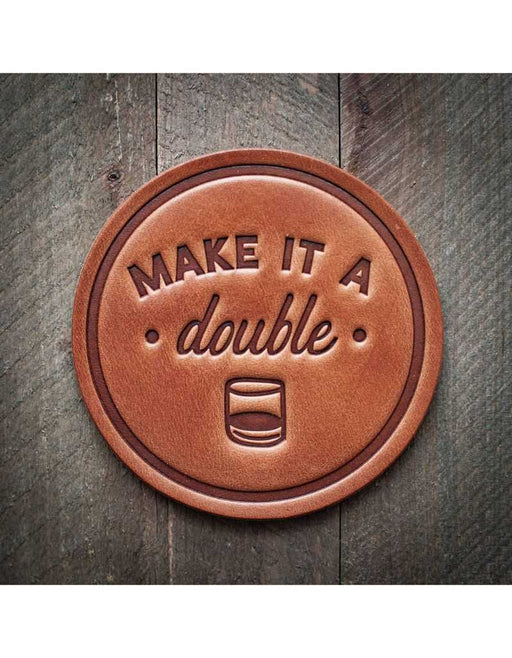 Brown leather coaster with 'MAKE IT A double' text on a wooden surface