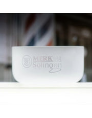 A frosted clear glass bowl with the text 'MERKUR Solingen' and a circular emblem printed on the front, set against a blurred background.