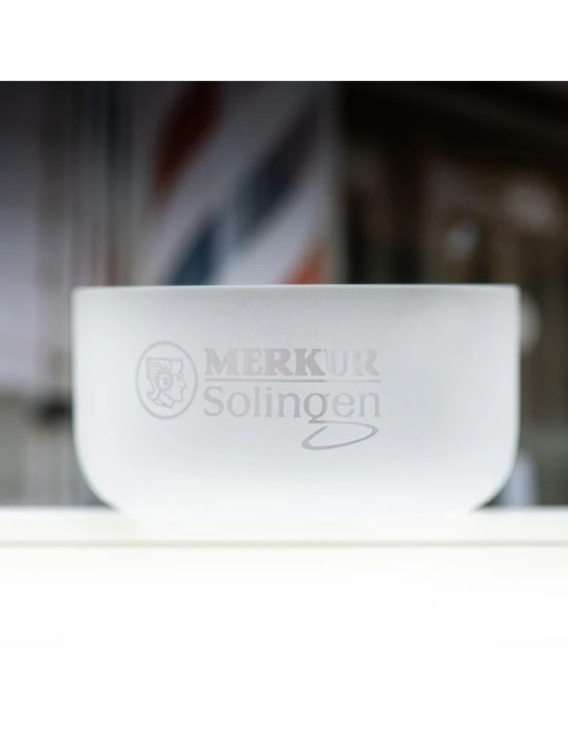 A frosted clear glass bowl with the text 'MERKUR Solingen' and a circular emblem printed on the front, set against a blurred background.
