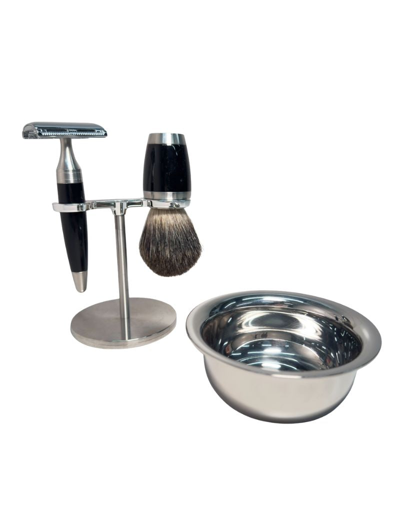 A luxury wet shaving kit featuring a stainless steel and black resin safety razor, a mixed badger hair brush, a stainless steel stand, and a stainless steel bowl, all displayed on a marble surface.