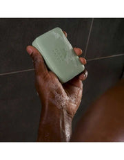 Hand holding green Epsom Salt Bar Soap lathered with soap suds