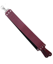 A red leather straight razor strop with metal hardware and paddle handles.