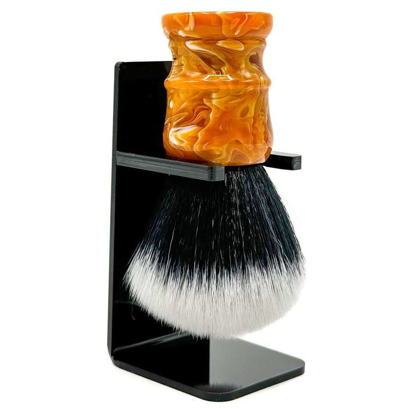 A premium synthetic bristles shaving brush with a marbled golden yellow, brown, and white resin handle, displayed with a black acrylic brush stand.