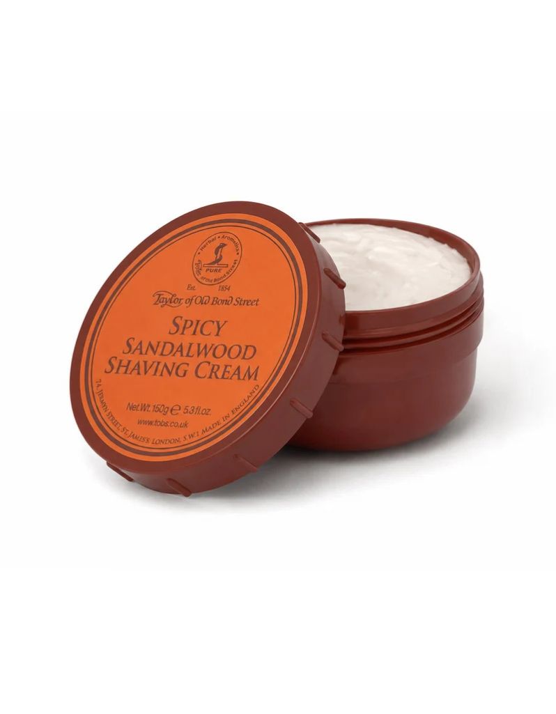 An open jar of Taylor of Old Bond Street Spicy Sandalwood Shaving Cream with its lid leaning against it, showing the white cream inside. The jar and lid are dark reddish-brown with a prominent orange label.