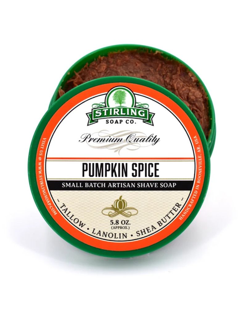 An open round green tin of Stirling Soap Co. Pumpkin Spice shave soap, showing the brown lather inside, with a detailed product label on a white background.