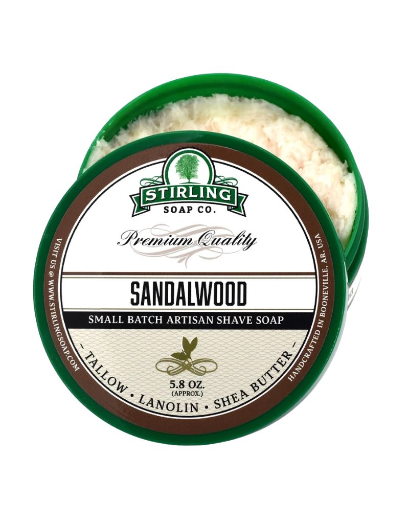 An open round green tin of Stirling Soap Co. Sandalwood Smoother Shave Soap, showing the white textured soap inside, with the front label facing forward on a white background.
