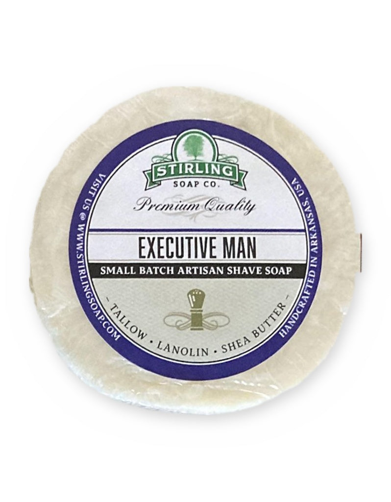 A single round bar of Stirling Soap Co. Executive Man artisan shave soap, wrapped in clear plastic with a prominent white, blue, and green paper label, set against a plain white background.