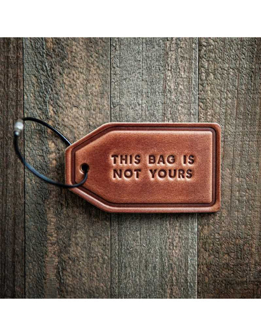 Brown leather luggage tag with 'This bag is not yours' text on a wooden surface